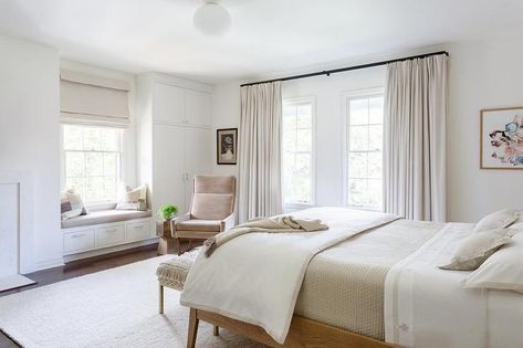 A pink velvet wingback chair sits in the corner of this calming, chic bedroom between a window covered in ivory curtains and a white built-in window seat topped with a gray cushion. White And Pink Bedding, Window Behind Bed, Curtains Behind Bed, Blue And White Bedding, White Loft Bed, Built In Window Seat, Pink Velvet Chair, Velvet Wingback Chair, Pink Bedroom For Girls