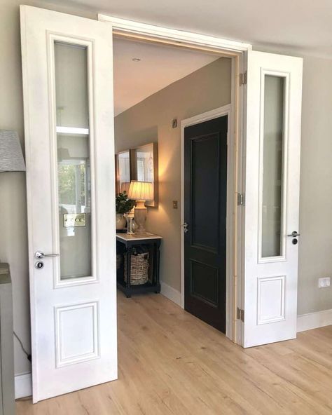 White double doors with glass are opened to reveal a hallway with light wood flooring. A two-toned black console table lit by recessed lights in the hallway stands next to a black interior door. Doors In Hallway, White Double Doors, Light Wood Flooring, Black Interior Door, Recessed Lights, Black Console Table, Moody Interiors, Doors With Glass, Light Wood Floors