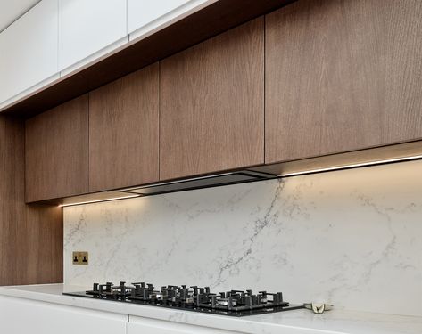 Downlighting over your prep area in your kitchen will make it easier for you to see when preparing a meal. It will also give the room a very contemporary and designed feel. To compliment this modern design, our client also chose to hide the extractor duct behind false cabinetry that matches real cabinets flanking the extractor hood. Concealed Hood Kitchen, Modern Extractor Hood Ideas, Modern Kitchen Extractor, Extractor Hood Ideas, Hide Kitchen, Kitchen Extractor Hood, Modern Kitchen Hood, New Kitchen Inspiration, Kitchen Extractor Fan