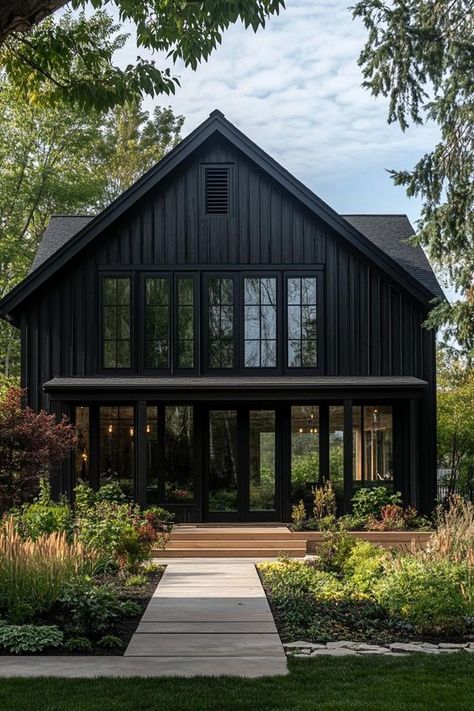 Modern barndominium house facade of black stained wood with black trim beautiful farmhouse garden landscape. Check out the coolest dark barndominium houses that combine rustic charm with modern sophistication, enhancing a living space with bold hues and sleek designs. Dark Exterior Cabin, Charcoal Grey Barndominium, Dark Houses Modern, Black Exterior Railing, Charcoal Siding House Exterior, Black Timber House, Board And Batten Siding Exterior, Dark Barndominium, Black Houses Exterior