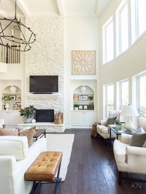 White Living Room Design with Statement Two Story Painted Stone Fireplace White Living Room Fireplace Ideas, White Stone Fireplace Living Room, White Chic Living Room, White High Ceiling Living Room, Living Room 2 Story Ceiling, 2 Story Family Room Fireplace, Tall Fireplace Design Ideas, Two Story Great Room Wall Decor Ideas, White Tall Fireplace