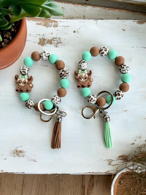 Cute highland cow beaded wristlet keychain. Highland cow with mint green bow, mint green silicone beads, brown and brown & white animal print beads. Includes a silver keychain with a lobster clasp and your choice of a brown or mint green tassel. Contains 15mm silicone beads. Show off the cute cowgirl style wristlet! This lightweight and durable wristlet slips easily over your wrist and the silicone beads are soft and comfortable. Treat yourself or buy as a gift for Mother's Day, birthdays, stock Beaded Wristlet Keychain, Silicone Bead Keychain, Cute Cowgirl, Cute Highland Cow, Beaded Wristlet, Keychain Craft, Silver Keychain, Beaded Keychain, Green Bows