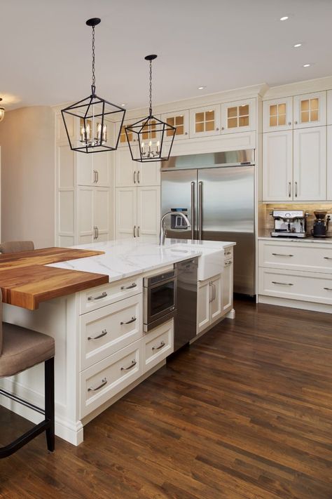 Traditional White Kitchen with White Shaker Cabinetry, Glass Insert Upper Cabinetry, Crown Moulding, Butcher Block & Granite Island with Distressed Hardwood Flooring. Designer: Michael Burr . . . . #kitchen #kitchendesign #kitcheninspo #kitchenrenovation #kitchenreno #traditionalkitchen #whitekitchen #whitecabinets #kitchenisland #glasscabinets Mixed Material Kitchen Island, Kitchen Island With Drawers And Seating, Butcher Block Island With Seating, White Kitchen With Butcher Block Island, Kitchen With Butcher Block Island, Traditional White Kitchen, Kitchen Island With Drawers, Kitchen Cabinets Color Combination, Granite Kitchen Island