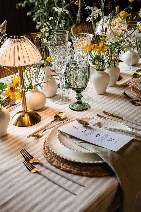 Striped tablecloth with wicker place mat with white plates, sage green napkins and monochrome wedding menu stationery with white and gold cutlery including green coloured glassware with small lamps and wildflowers in white vases | wedding table decor | green and yellow wedding colour palette | Jacqui McSweeny Sage Green Wedding Tablescape, Green Glasses Wedding, Colourful Table Setting Wedding, Yellow Green White Color Palette, Sage Green White And Yellow Wedding, Green And White Wedding Palette, Table Lamps Wedding Decor, Green Yellow White Wedding, Forest Green And Yellow Wedding