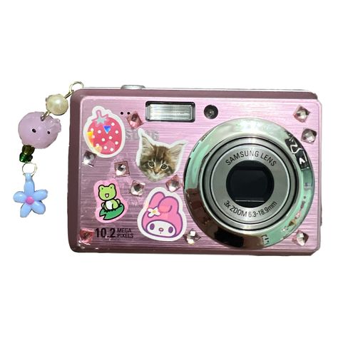 It’s a pink digital Samsung camera with cute stickers placed onto it (my melody, a frog, a cat, and a strawberry) as well as light pink and purple jewels. To the left of it dangles 4 charms connected together by metal loops. The charms are a blue flower, two green small beads, a tiny white pearl, and pink pig bead made of glass Digital Camera Png Aesthetic, Y2k Camera Png, Digital Camera Deco, Digital Camera Stickers, Camera Stickers Aesthetic, Decorated Camera, Cute Camera Icon, Camera With Stickers, Digital Camera Png