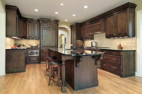 Truly dark wooden cabinets and island, along with black countertops, work with the light natural flooring and tile backsplash in this contrasting kitchen. Modern Walnut Kitchen, Walnut Kitchen Cabinets, Dark Wood Kitchen Cabinets, Traditional Kitchen Cabinets, Model Dapur, Dark Wood Kitchens, Wood Floor Kitchen, Walnut Kitchen, Oak Kitchen Cabinets