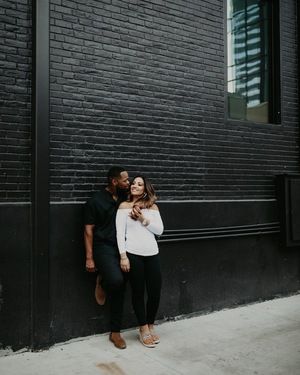 Couple-resting-against-a-black-brick-wall-in-Austin-TX-for-their-outdoor-engagement-photoshoot Engagement Photos With Brick Wall, Brick Wall Engagement Pictures, Winter Engagement Photos With Dog, Anniversary Photography Poses, Sitting In The Park, Anniversary Photography, Wedding Anniversary Photos, Engagement Photography Poses, Photos With Dog