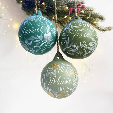 These gorgeous green baubles are a perfect keepsake and can be personalised with a name of your choice! Ceramic bauble hand painted with any name, and in a choice of 3 glorious greens!The price shown is per bauble Choose from three colours:Harriet: Winter green with silver flowersEvie: Olive green with snowdrop illustrationMaisie: Sage green with gold flowers Ceramic bauble, paints and calligraphy inks, varnish Diy Painted Baubles, Personalised Ornaments Christmas, First Christmas Bauble, Snowdrop Illustration, Hand Painted Baubles, Painted Baubles, Hand Painted Bauble, Flowers Ceramic, Winter Green