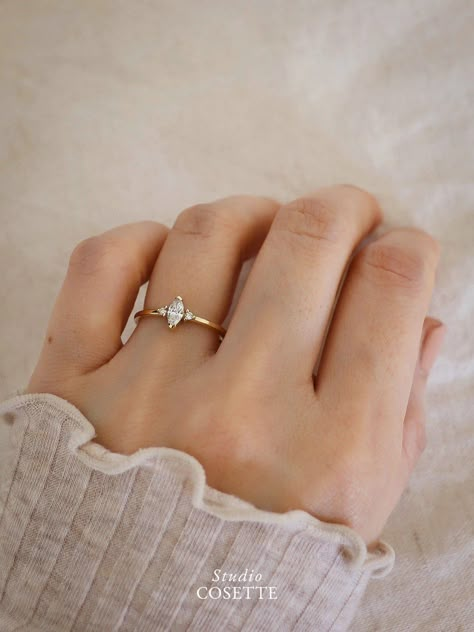 Our Florence ring is inspired by a vintage approach: a three-stone diamond ring with a petal-like Marquise diamond in the center and two sparkling side diamonds. The ring is timeless, minimal, with a tiny bit of whimsy—making it the perfect engagement ring! Available in 0.20ct and 0.50 ct For 0.20 ct Made of yellow gold or white gold. 1 x Lab grown Marquise diamond. Size: 6x3 mm (~0.20ct). F color and VS Clarity. 2 x Lab grown side diamonds. Size 1.5 mm each. Band 1.3 mm in width and thickness. Minimalist Engagement Ring Solitaire, Dainty Wedding Rings White Gold, Marquise Engagement Ring Minimalist, Simple Boho Engagement Ring, Marquise Engagement Ring Dainty, Unique Dainty Wedding Rings, Dainty Moissanite Engagement Ring, Tiny Diamond Engagement Ring, Dainty Solitaire Engagement Ring