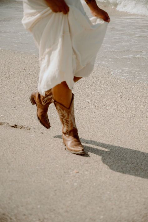 Florida based wedding and couples photographer captures a Coastal Cowgirl themed portrait session at Manasota Key, FL showing her in an olive green bikini with a knitted sweater, flowing white skirt, and cowgirl boots in the sand. #coastalcowgirl #countrybeachsession #beachportraitsession #coastalcowgirlphotoshootideas #floridaportraitphotographer Coastal Cowgirl Couple Photoshoot, Coastal Cowgirl Engagement Photos, Beach Cowgirl Photoshoot, Coastal Cowgirl Wedding Aesthetic, Coastal Cowgirl Theme, Coastal Cowgirl Photoshoot, Skirt And Cowgirl Boots, Coastal Cowgirl Wedding, Costal Cowgirl Aesthetic