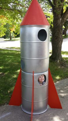 A play rocket that I made from two 55 gallon drums, a paper cone and MDF wings held on with lattice channel. Rocket Ship Trunk Or Treat, Rocket Ship Decorations, Space Themed Parade Float, Outerspace Classroom Decor, Space Camp Decorations, Diy Rocket Ship Cardboard, Diy Space Shuttle, Diy Rocketship, Diy Space Decorations