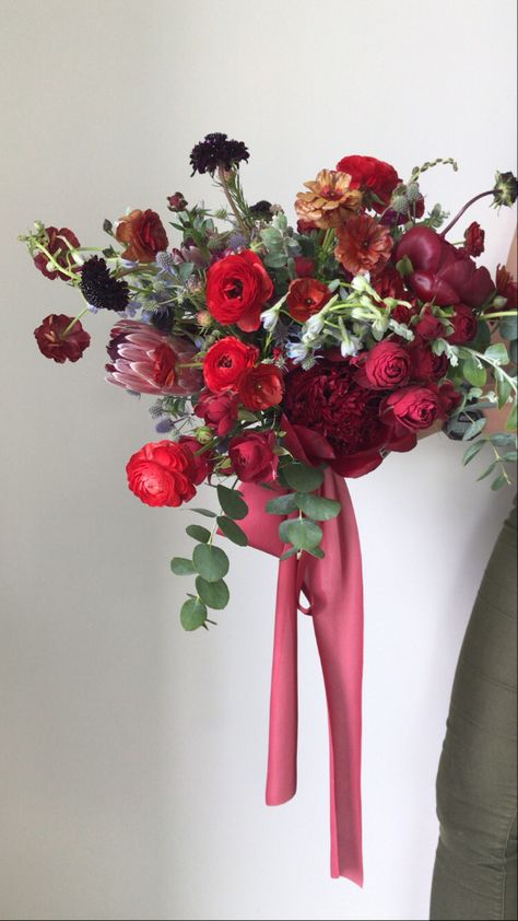 This airy bridal bouquet is filled with juicy blooms like peonies, ranunculus, thistle,  and protea. The red tones are bold but romantic and pop perfectly against the subtle blues. Designed by Frenchie’s Floral Studio. Red Ranunculus Bouquet, Ranunculus Bouquet, Bridal Bouquet Summer, Floral Studio, Ranunculus, Jewel Tones, Peonies, Bridal Bouquet, Getting Married