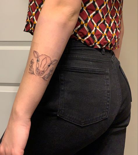 Girl is wearing black high waisted jeans with a cropped red, orange, and yellow checkered shirt facing her back towards the camera. Her left arm is facing the camera where the tattoo of a thinly lined cow head surrounded by two rose buds symmetrically on either side is shown. The tattoo is placed 3 inches below her elbow. Cow And Pig Tattoo, Tattoo Lines, Bicep Tattoo Women, Lamb Tattoo, Aa Tattoos, Pig Tattoo, Cow Tattoo, Back Of Arm Tattoo, Vegan Tattoo