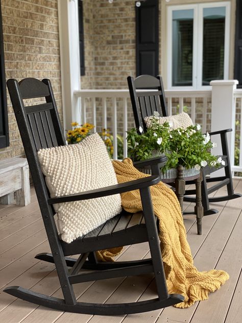 Front porch with black rocking chairs and a mustard yellow blanket, coat cream pillows and flowers. Porch With Black Rocking Chairs, Black Chairs Front Porch, Yellow House Front Porch, Black Porch Rocking Chairs, Black Outdoor Rocking Chairs, Rocking Chair On Porch Decor, Colorful Rocking Chair Front Porches, Farmhouse Rocking Chair Front Porch, Rocking Chair Patio Ideas