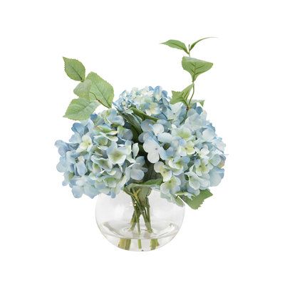 Bring the beauty of nature to the comfort of your own home. Featuring an elegantly crafted blue hydrangea arrangement with a realistic look of acrylic water in a clear bubble bowl glass. Our faux plant will bring you the joy and beauty of the outdoors without any watering necessary. | Creative Displays, Inc. Hydrangea Floral Arrangements & Centerpieces in Vase Plastic / Polysilk in Green | 11 H x 12 W x 16 D in | Wayfair Small Hydrangea Arrangements, Hydrangea Small Centerpiece, Blue Flower Arrangements Table, Simple Hydrangea Centerpiece, Blue And White Hydrangea Centerpiece, Hydrangea Table Centerpiece, Hydrangea Wedding Centerpieces, Baby Shower Centerpieces For Boys, Blue Hydrangea Centerpieces