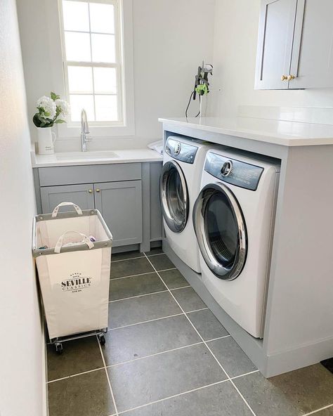 These light gray laundry room cabinets are topped by a white countertop. The room is finished with gray rectangular floor tiles. Enclose your washer and dryer under a gray counter with a white countertop to create a nifty folding station in a small space. Counter On Top Of Washer And Dryer, Laundry Layout Ideas, Light Gray Laundry Room, Gray Laundry Room Cabinets, Laundry Layout, Gray Laundry Room, Folding Station, Small Laundry Space, Grey Laundry Rooms