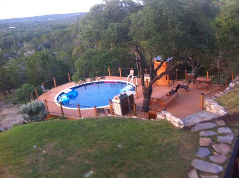 Above ground pool deck in the Texas Hill Country. Two level deck with outdoor kitchen and rustic cedar changing room on the pool level. It features stone retaining walls, with a flagstone staircase leading from the yard to the upper level deck. Above Ground Pool On Hill, Pool In Hillside, Outdoorsy Decor, Hillside Pool, Raised Pools, Two Level Deck, Outdoor Deck Decorating, Above Ground Pool Deck, Pool Pond