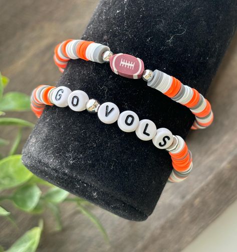 Cheer on your team in style with our football stadium stack bracelets, featuring clay and acrylic beads in your favorite team's colors. Perfect for game day and tailgating, these vibrant accessories add a touch of spirited flair to any outfit. Product Details: ~Handmade and Made to order ~Bracelets measure 7" each perfect for most adults and teens. ~ Please understand the actual color may very slightly from your monitor. ~All letters are uppercase. ~Heishi, Acrylic, and  Silver or Gold Filled Beads ~Beads are placed on a flexible elastic/stretchy cord. Product Care: ~Roll bracelets on to avoid over stretching.  ~Avoid contact with water, oils, perfumes, chemicals and creams to improve longevity. Please use adult supervision in children under 3, and don't let children put the bracelets in t Clay Bead Bracelet Ideas Football, White Beaded Bracelets For Sports Events, White Beaded Bracelets For Football Season, Clay Bead Bracelet Ideas, Letter Bead Bracelet, Bead Bracelet Ideas, Vibrant Accessories, Bracelet Business, Football Jewelry