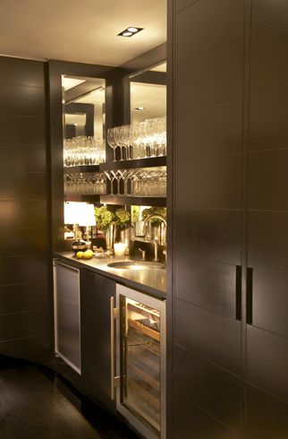 Sleek modern wet bar with espresso cabinetry. The bar area is flanked by cabinets, it features a mirrored interior and espresso stained floating shelves for glasses. A built-in mini fridge and glass fronted wine fridge sit below the counter. A black countertop is paired with an undermount bar sink and polished nickel faucet. Paul Davis - New York Modern Wet Bar, Modern Bar Cabinet, Espresso Cabinets, Home Bar Areas, Built In Bar, Home Bar Designs, Mini Bars, Bar Sink, Bar Interior