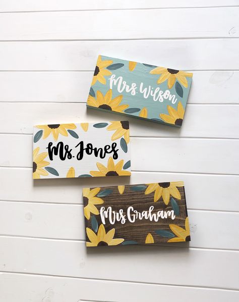 "Sunflower Teacher Name Sign  Cute to sit on a desk or shelf (can stand alone) or request to have a twine hanger attached to hang the sign on a hook or doorknob  Hand lettered name- hand painted flowers No two signs are exactly alike! No stencils used  Wooden sign measures approximately 5.5 by 10 by 1 inches  If you have a longer name, you can order this \"add on\" listing to make it 14 inches long instead of 10 inches long. Message me with any questions. Link,  https://etsy.me/2SJ67K4   Choose Sunflower Classroom, Painted Name Signs, Teacher Desk Signs, Teacher Classroom Sign, Teacher Door Sign, Teacher Canvas, Teacher Door Signs, Teacher Door Hangers, Teacher Name Signs