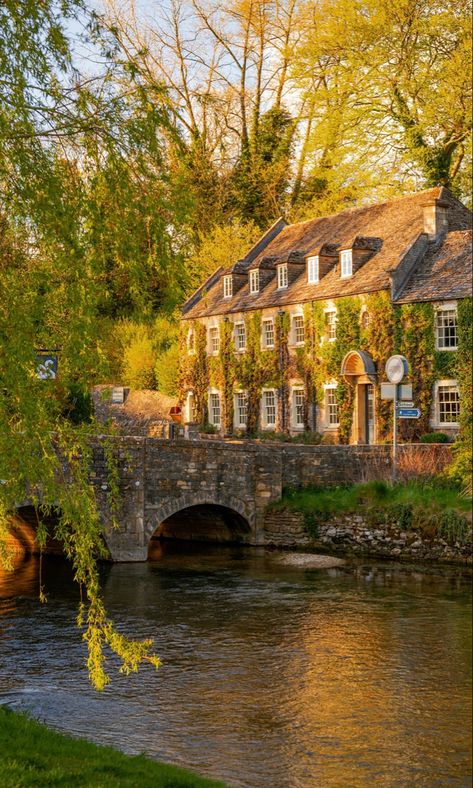 A period property in the evening sunshine behind a river and small road bridge. The spring scene is surrounded by trees that are beginning to bloom. England Aesthetic, England Countryside, Cotswolds England, Castle Combe, Voyage Europe, The Cotswolds, English Countryside, England Travel, Uk Travel