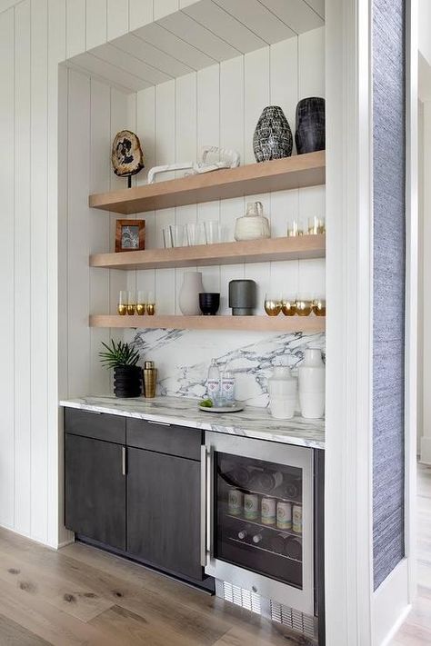 Well-appointed bar nook is fitted with floating blond wood shelves stacked against a white shiplap backsplash over black cabinets and a glass front beverage fridge fixed beneath a black and white marble countertop fitted against a black and white marble backsplash. Small Home Bar Ideas, Small Wet Bar, Wine And Coffee Bar, Small Bars For Home, Bar Nook, Home Wet Bar, Home Bar Rooms, Coffee Bar Design, Home Bar Design