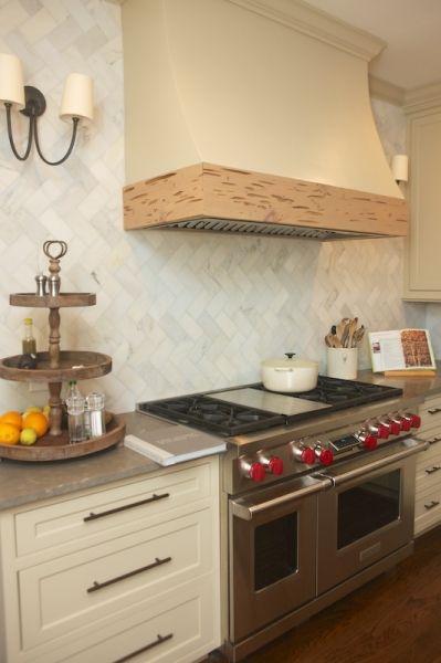 Kitchen features cream cabinets paired with gray countertops and herringbone marble backsplash as well as cream kitchen hood accented with wood trim over Wolf Range. Cream Herringbone Backsplash, Herringbone Backsplash Kitchen, Marble Herringbone Tile, Built In China Cabinet, Herringbone Tile Backsplash, Cream Kitchen Cabinets, Tile Countertops Kitchen, Trendy Kitchen Tile, Marble Herringbone