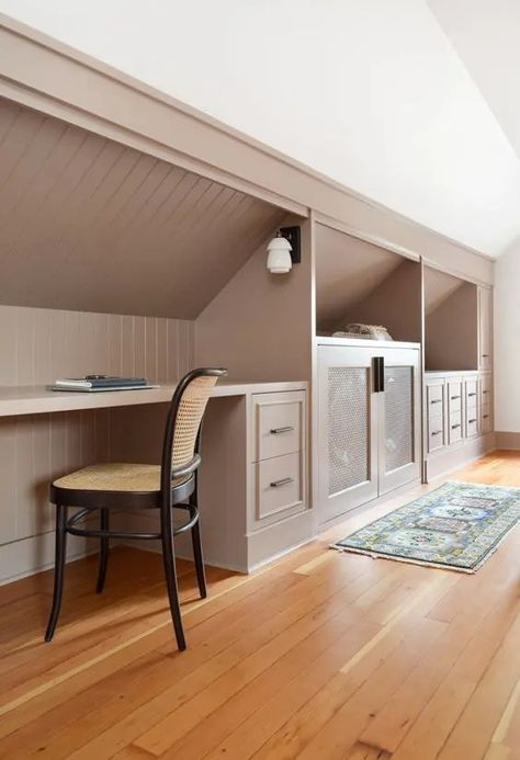 a cool attic space featuring built in storage with drawers and cabinets, a desk and a cane chair looks awesome Slanted Ceiling Home Office, Built In With Slanted Ceiling, Wood Panel Attic, Angled Ceiling Storage, Office Attic Ideas, Dormer Storage, Eaves Storage Ideas, Attic Office Space, Attic Built Ins