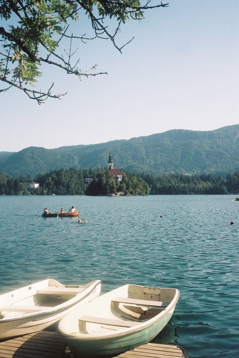 A photo of Lake Bled, the Island is in the distance. Two white rowing boats are by the side of the water Lake Bled Aesthetic, Inter Railing, Lake Bled Slovenia, Cool City, 35mm Film Photography, Bled Slovenia, Slovenia Travel, Unique Wedding Photography, Lake Bled