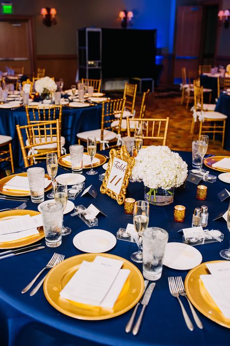 Navy Blue and Gold Ballroom Wedding Reception Table Decor with Blue Satin Linen, Gold CHargers, Stylish Gold Framed Table Number, and Small White Hydrangea Centerpiece in Glass Cylinder Vase | Tampa Bay Wedding Rental Company Gabro Event Services | Hyatt Regency Clearwater Beach Navy And Gold Centerpieces Diy, Wedding Linens Ideas Color Schemes, Navy Blue White And Gold Wedding Table Settings, Navy Blue And Gold Centerpieces, Royal Blue And Gold Party Decorations, Royal Blue Table Setting, Blue Gold And White Wedding, Blue And Gold Wedding Theme, Table Decorations Blue