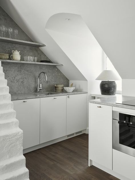 "When it came to redesigning the kitchen, slanted ceilings meant that all appliances had to be below the counter," Nydahl describes. "We forwent overhead cabinets in favor of open shelving to maximize the space, also adding a pretty impactful design moment (the bottom shelf also has integrated lighting for added functionality)."  Credit: <a href="https://kristoferjohnsson.com/">Kristofer Johnsson</a> Minimal White Kitchen, Kitchens White, White Kitchen Inspiration, Limestone Countertops, White Washed Floors, Kitchen Architecture, Stockholm Apartment, White Shaker Kitchen, Minimal Kitchen