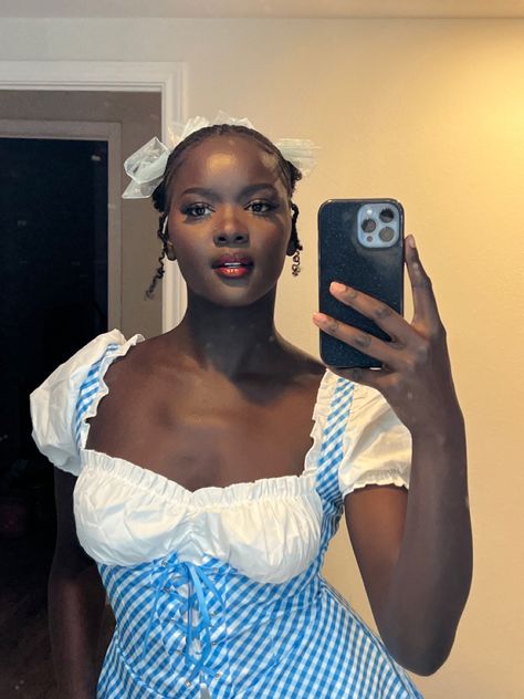 Dark skin black woman taking a photo in the mirror with a Dorothy halloween costume on. She has two space buns with a blue bow on each one. She has red lipstick and has a semi-serious look Dorothy Costume Makeup, Dorothy Makeup, Dorothy Hair, Dorothy Halloween Costume, Dorothy Costume, Cool Makeup Looks, Halloween 2024, Hallows Eve, Halloween Outfits