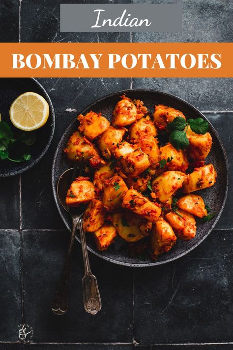 bombay potatoes served in a black bowl with two serving spoons Bombay Aloo Recipe, Indian Mint Sauce, Bombay Potato Recipe, Indian Potato Recipes, Indian Takeout, Spicy Potatoes, Homemade Curry Powder, Bombay Potatoes, Indian Side Dishes