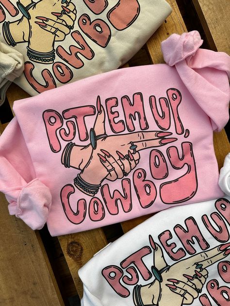 "Put Em Up, Cowboy" Sweatshirt Available in White, Pink & Cream Available in Crew Neck or Cut Out Neck Oversized & Slouchy Style ~ size down if you want it more fitted Super Soft 50% Cotton 50% Polyester Runs True Small 0/2/4 Medium 4/6/8 Large 8/10/12 XL 12/14/16 2XL 16/18/20 3XL 20/22/24 ***These Are PRINTED/MADE TO ORDER! Please Allow 7-10 Business Days To Ship. If You Order Multiple Items, These Will Be Shipping Out SEPARATELY From Your Order. Fun T Shirts For Women Graphic Tees, Funny Cowboy Shirts, Western Boutique Names, Birthday Gift Ideas For Women, Cowboy Print, Cowgirl Gifts, Slouchy Style, Cute Shirt Designs, Vinyl Shirts