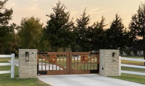 Farmhouse-style homes deserve complementary driveway gates. Wood can be hard to maintain. Our answer is faux-wood painted aluminum gates. Check out more of our designs and then contact us to design something specific for your estate. This faux-wood painted custom aluminum gate decorated for fall is a simple example of one of our designs. Gate Design Driveway, Gated Ranch Entrance, Diy Entrance Gate, Farm Gate Entrance Ideas, Ranch Entryway Driveway, Carport Gate Ideas, Gated Entrance Driveway, Fence Entrance Ideas, Big Gates Entrance