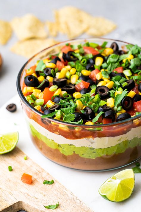 Vegan 7 Layer Dip Recipe layered with guacamole, beans, salsa, sour cream, corn, tomatoes and olives is a great centerpiece for everyone to gather around. Perfect snack for sport events, movie night or any casual get together with family and friends. Easy, healthy and ready in under 15 minutes. #veganrecipes #sevenlayerdip #healthyrecipes #healthybeandip #wfpb Vegan Layered Bean Dip, Layered Bean Dip Recipe, Layer Dip Recipe, 7 Layer Dip Recipe, Bean Dip Recipe, Layered Dip Recipes, Layered Bean Dip, 7 Layer Dip, Vegan Dips