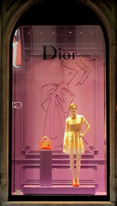 When I speak of the term color, the designer use bold colors such as yellow, orange and light purple. The dress and the purse stands out. For scale, it is comparing the size of the purse to the mannequin standing next to it. The purse is very small, whereas the mannequin is tall. Line and composition is represented in the background with the drawing of the dress behind the mannequin and purse. It looks like the shape of a dress women would wear in the old days Fashion Window Display, Vitrine Design, Window Shopper, Clothing Store Design, Store Design Boutique, Visual Merchandising Displays, Window Display Design, Store Window, Retail Store Design