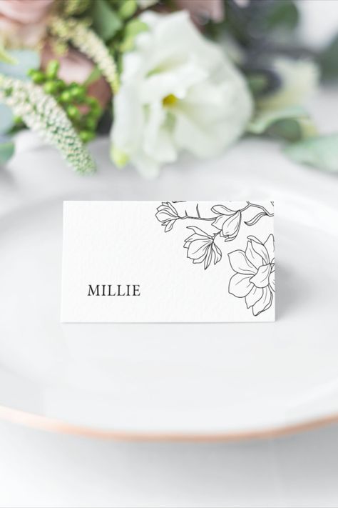 Black line drawn magnolia flower print tent fold style place card. Shown on a white plate Wedding Place Cards Flowers, Magnolia Place Cards, Flower Name Place Cards, Wedding Name Place Cards Flower, Wedding Name Place Cards Calligraphy, Handwritten Place Cards, Place Name Cards, Place Setting Cards, Magnolia Collection