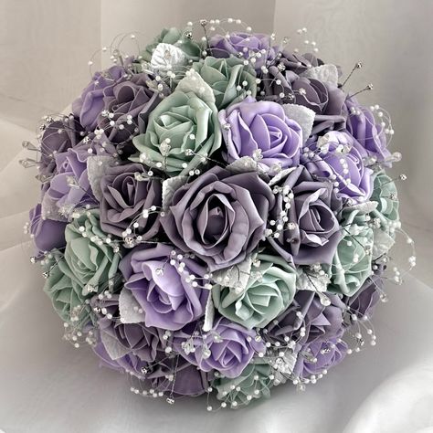 "Affordable Artificial Wedding Bouquet with Sage Green, Lavender & Lilac Roses with Diamantés, Pearls and Crystals. A beautiful sparkling handmade bridal bouquet, created using high quality artificial sage green, lavender and lilac foam roses. I have incorporated crystals, pearl sprays and diamantes with small white leaves mingled throughout the bouquet. The handle has then been wrapped in lilac satin ribbon with a small ribbon bow. A lovely wedding bouquet to complement your sage green and lavender wedding theme.  These wedding bouquets are available in 3 sizes and many colours. All at very low prices. I have bouquets to suit all budgets. Please see my other listings for different colours, or message me, to enquire about any colour.  If you require a different colour ribbon on your bouque Bouquet Sage Green, Lilac Wedding Themes, Sage Green Wedding Theme, Roses Bridal Bouquet, Flowers Bridesmaids, Lavender Wedding Theme, Sage Green Flowers, Purple And Green Wedding, Lilac Bouquet