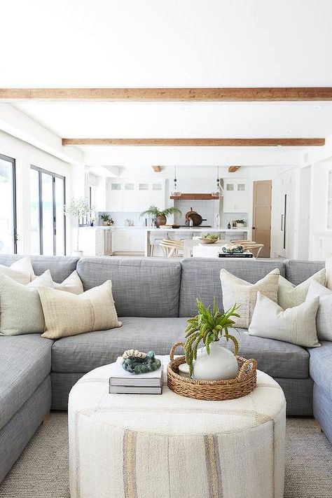 A round ivory ottoman coffee table sits on a gray rug in front of a blue-gray u-shaped sectional accented with ivory pillows. Pure Salt Interiors, Pure Salt, Apartment Decoration, Grey Sectional, Cottage Living Rooms, Ottoman Coffee, U Shaped Sectional, Coastal Living Room, Gray Rug