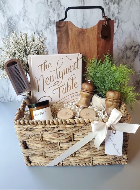 A charming custom wedding gift basket for a beautiful new couple celebrating their special day! Filled with some rustic items for their new home and a cookbook to inspire couples to cook as a team! #weddinggiftideas #weddinggiftideas #weddinggiftbasket #weddinggiftbasketideas #giftsforcouples Move In Gift Basket Ideas, Newly Wed Gifts Ideas Couple, Game Night Wedding Gift Basket, Gift Basket With Purse, Newlywed Basket Ideas, Engagement Party Basket Gift, Wedding Shower Basket Ideas, Bridal Shower Box Gift, Bride And Groom Gift Basket