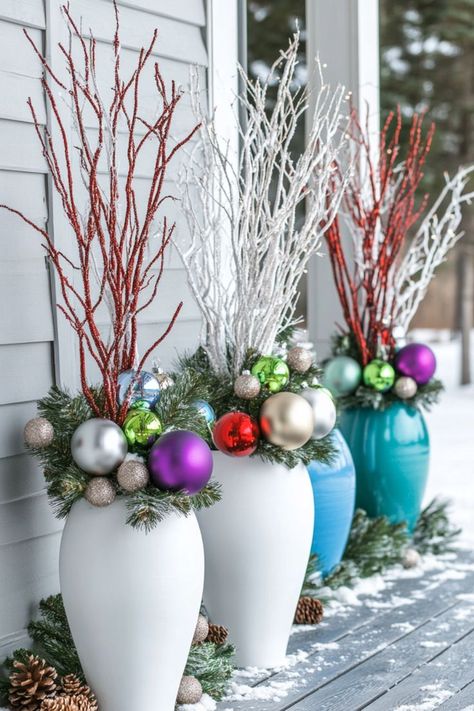 White and blue vases feature festive arrangements of colorful ornaments, pine branches, and red and white twigs, set on a snowy wooden porch. Christmas Porch Planters Diy, Cheap Christmas Porch Decor, Diy Christmas Pots Outside, Diy Christmas Planter Ideas, Outdoor Christmas Planters Winter Porch Front Doors, Winter Wonderland Outside Decorations, Christmas Garden Decorations Outdoor, Gnome Christmas Decor Ideas, Holiday Planter Ideas