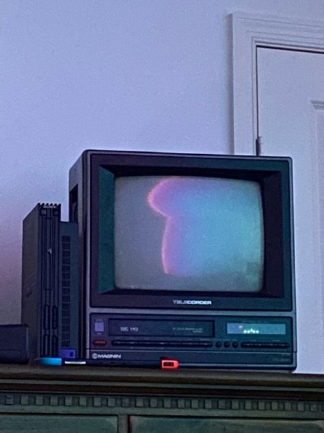 An 80s tube tv sitting on a wooden dresser, the screen is off and the reflection shows cool colored lights in the room. Next to it is a ps2, in front of it is a switch Old Tv Wallpaper, Tv Asthetic Picture, 2000s Tv Aesthetic, Old Television Aesthetic, Vhs Tv Aesthetic, 90s Tv Set, Games To Install On Your Phone, 80s Tv Aesthetic, Box Tv Aesthetic