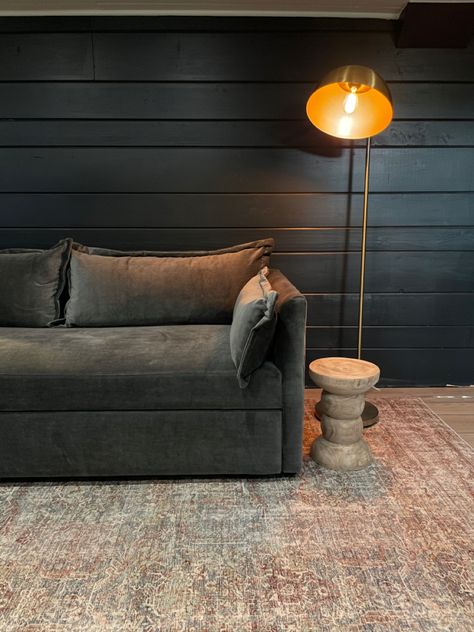 Black shiplap, living room with charcoal velvet couch and amber lamp Dark Office Wallpaper, Dark Moody Tv Room, Moody Family Room Cozy, Moody Grey Living Room, Moody Open Concept Living Room, Small Tv Room Design, Dark Living Rooms Cozy, Modern Tv Room Design, Moody Tv Room