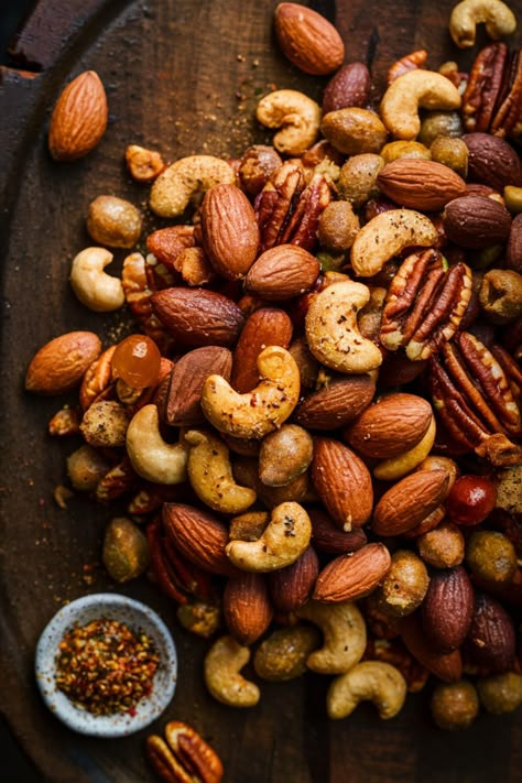 Mixed nuts with seasoning on a wooden surface, including almonds, cashews, and pecans. A small bowl of seasoning is on the side. Spiced Nut Recipes, Smoked Snacks Recipes, Smoked Nuts Recipes, Smoked Nuts And Bolts, Seasoned Nuts Recipe Savory, Smoked Nuts In Smoker, Spiced Nuts Recipe Savory, Seasoned Nuts Recipe, Smoked Cashews