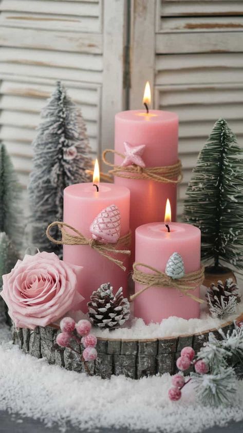 A beautiful and cozy winter-themed arrangement. At the center, there are three pink pillar candles of varying heights, each decorated with twine and delicate holiday ornaments such as pink and silver pinecone-shaped decorations and a small pink star ornament. The candles are lit, casting a warm, soft glow. Pink Christmas Table Centerpieces, Pink Christmas Candles, Desk Themes, Pink Christmas Table Setting, Pink Christmas Bedroom, Pink Pillar Candles, Pink Shabby Chic Christmas, Christmas Tree Roses, Pink Christmas Table