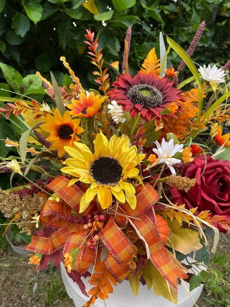 Welcome the fall season with a colorful tall arrangement for your foyer table, side table, mantel or large countertop.  The arrangement measures approximately 20"H, 12" D, 14" W  from tip to tip in a handmade, walnut stained 7"x7"x 4" wooden  container and is generously loaded with fall greenery, a large burgundy and yellow sunflower, a large deep red rose, white daisies, mini sunflowers, fall accent flowers in yellow, orange and burgundy with a small pumpkin and a colorful plaid loopy bow. We offer the wooden container in a variety of colors. Please select before completing your order.    Custom floral work is welcomed.  If ordering multiple arrangements for a wedding or special event, please feel free to message me for pricing and the timeline needed to complete the order. If sending as Fall Flower Arrangements For Church, Sunflower Table Decor, Fall Dining Table Decor, Sunflower Floral Arrangements, Floral Table Decor, Fall Pots, Sunflower Table, Fall Greenery, Fall Dining Table