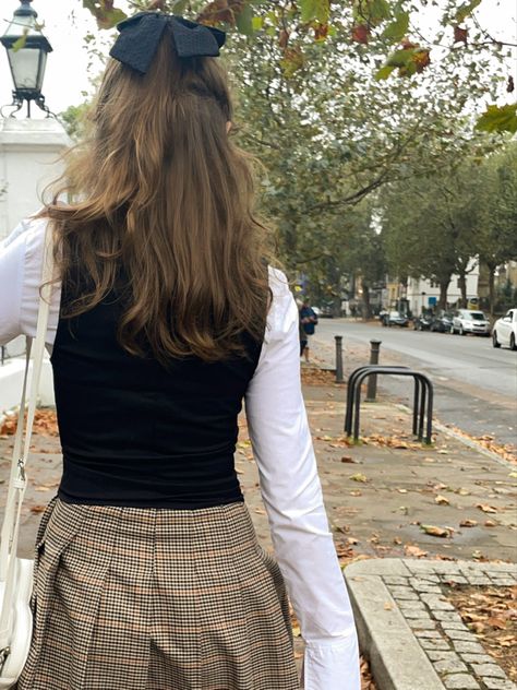 girl wearing white shirt under a black waistcoat, a plaid checked brown skirt with a heart shaped bag with a black bow clip in her hair walks down an autumnal london street Preppy Light Academia Outfits, Girly Dark Academia, Light Academia Skirt, Light Academia Aesthetic Outfit, Dark Academia Aesthetic Outfit, Light Academia Outfit, 6th Form Outfits, Sixth Form Outfits, Dark Academia Outfits