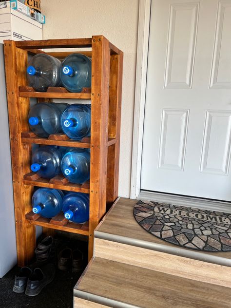 Handy way to store bottles and save space Water Cooler Bottle Storage, How To Store 5 Gallon Water Jugs, Diy 5 Gallon Water Bottle Storage, 5 Gallon Water Jug Ideas Diy Storage, Water Gallon Storage Ideas, Diy Water Jug Stand, 5 Gallon Water Bottle Storage, Water Jug Storage, Water Bottle Storage Rack