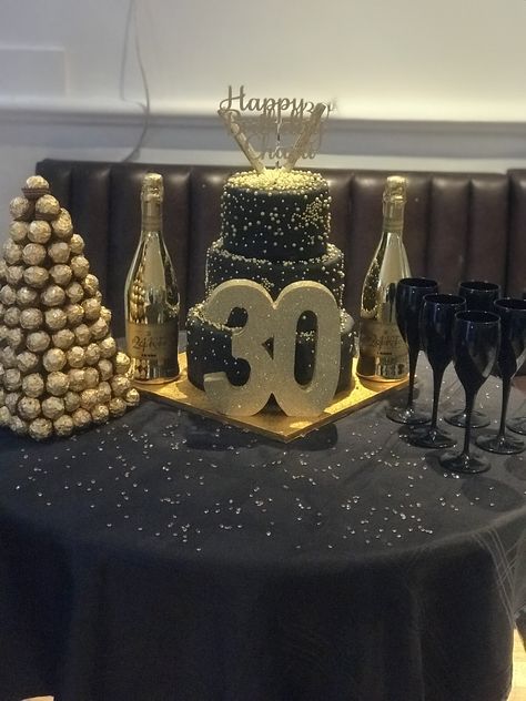 Cake table with gold champagne bottles, black champagne flutes and ferrero rocher tree! Black And Gold Cake Table, Gold Cake Table, Ferrero Rocher Tree, Black Champagne Flutes, Cake Table Decorations Birthday, Gold Table Centerpieces, Black And Gold Birthday Cake, Gold Candy Buffet, Gold Champagne Bottle